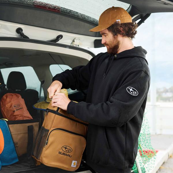 Photo of a man opening a Subaru-branded Carhartt bag in the open trunk of his car